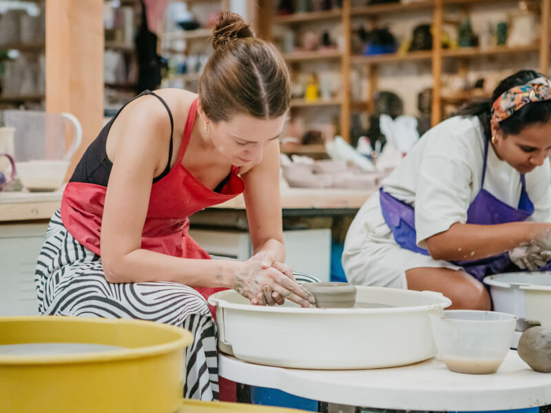 Two women sitting behind pottery wheels shaping clay